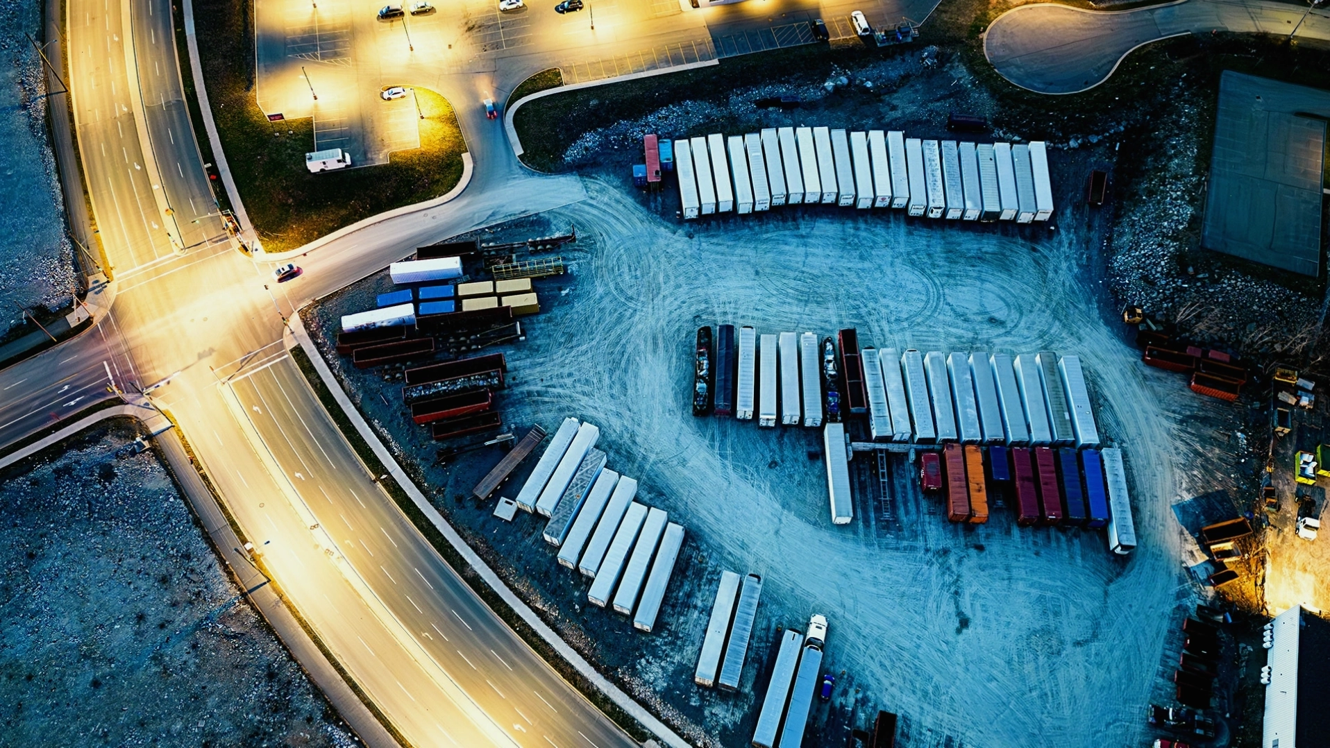 Hình ảnh từ trên cao về một bãi xe logistics vào lúc hoàng hôn với nhiều xe tải và container